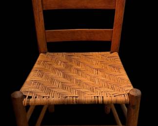 This rustic wooden ladder-back chair features a classic turned post frame and a tightly woven herringbone splint seat.