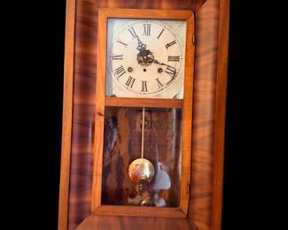 an antique American ogee (OG) wall or shelf clock featuring a mahogany or faux-flame veneer frame, a cream-colored dial with Roman numerals, and a visible swinging pendulum behind a lower glass panel