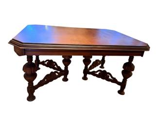 This is an antique Jacobean Revival carved wood dining table, likely dating from the 1920s to 1940s. It has two leaves.  