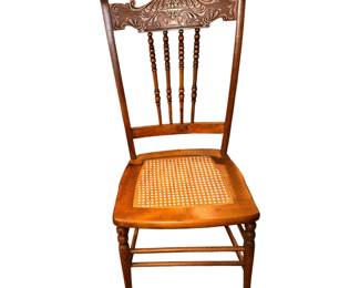 This is  an antique pressed-back oak chair featuring a woven cane seat and turned spindles, commonly produced during the late 19th to early 20th century.