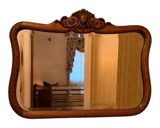 This is an antique oak beveled mirror featuring an ornate floral or scroll crest at the top and a curved wooden frame
