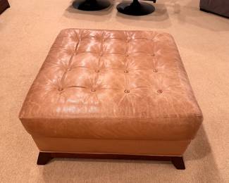 Tan leather tufted ottoman with wood base.