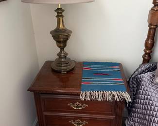 Cherry three drawer nightstand with brass table lamp and woven table runner