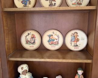 Hummel annual collector plates and Hummel figurines displayed in wood cabinet