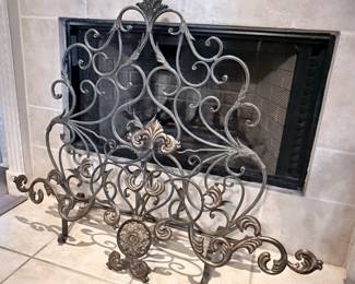 Ornate Fireplace Screen – Decorative metal fireplace screen featuring intricate scrollwork, fleur-de-lis accents, and an antique bronze finish. A beautiful functional accent for a fireplace, adding both style and protection to a living room or family room. Sold as found.