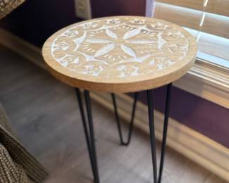 Carved Accent Table – Round accent table featuring a carved wood top with a decorative floral medallion design and black metal hairpin legs. A stylish accent piece for a living room, bedroom, or entryway. Sold as found.