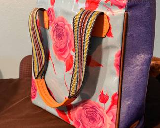 Consuela Tote Bag – Consuela tote bag featuring a floral print exterior, blue side panels, striped woven handles, and leather trim. A colorful everyday bag with the brand's signature style, perfect for work, travel, or daily use. Sold as found.