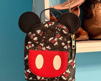 Disney Mickey Mouse Mini Backpack – Disney mini backpack featuring Mickey Mouse ear accents, an allover Mickey print, signature red front pocket, top handle, and gold-tone chain straps. A fun accessory for Disney fans, theme park visits, or everyday use. Sold as found.