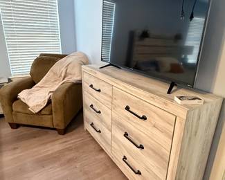 Light wood six-drawer dresser topped with a flat-screen television, paired with a coordinating upholstered accent chair. A versatile combination for a bedroom, guest room, or living space.