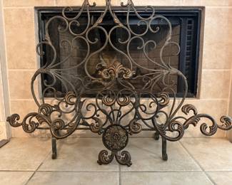Ornate Fireplace Screen – Decorative metal fireplace screen featuring intricate scrollwork, fleur-de-lis accents, and an antique bronze finish. A beautiful functional accent for a fireplace, adding both style and protection to a living room or family room. Sold as found.
