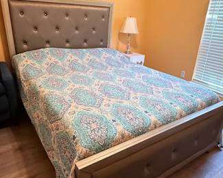 Upholstered bed featuring a tufted headboard and matching footboard, white one-drawer nightstand, crystal-style table lamp, and decorative accessories. A coordinated collection for a primary or guest bedroom. Items sold individually unless noted.