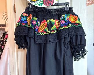 Embroidered Dress & Hand-Painted Hat – Black off-the-shoulder dress featuring colorful floral embroidery, lace trim, and ruffle details. Paired with a hand-painted hat decorated with a butterfly, roses, and floral accents. A vibrant set perfect for fiestas, cultural events, or themed celebrations. Items sold individually unless noted.