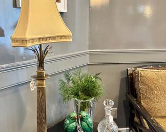 Left to right ($300 - Maitland-Smith neoclassical table lamp, 39” tall) ($400 - Pair of vintage Chinese Sancai green glazed ceramic parrots, 9” tall) ($110 - Waterford crystal metra face, 10” tall) ( $58 - Crystal wine decanter, 10” tall)