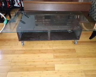 Industrial modern coffee table featuring thick tempered safety glass top on utility caster wheels.
