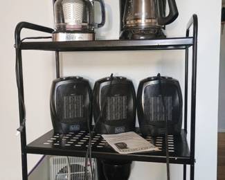 5-tier black metal utility display shelf loaded with personal space heaters and coffee makers.
