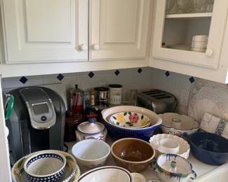 Blue and white ceramic mixing and serving bowl lot
Condition: Good
Mixed lot of blue-and-white ceramic kitchenware including several bowls, nesting-style bowls, serving bowls, and a few plates/covers visible in the cabinet and on the counter. Decorative motifs include floral transfers, scalloped rims, and solid blue-glaze pieces. No consistent matching pattern is evident across the group.