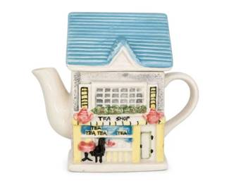 Ceramic cottage tea shop house teapot
Condition: Good
Decorative ceramic teapot shaped like a small tea shop/cottage house, with cream body, blue ribbed roof, painted storefront windows, and 'TEA SHOP' lettering on the front. Likely a novelty serving/display teapot rather than a daily-use kitchen piece.
