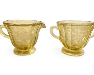 Amber pressed-glass handled creamer/pitcher pair
Condition: Good
Two matching amber glass small handled pitchers/creamers with pedestal bases and decorative pressed patterning. Likely vintage pressed/depression glass. No obvious chips or cracks are visible from the photo, but underside details are not shown.