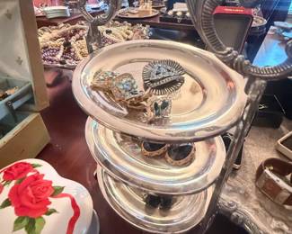 Ornate silver-plated 3-tier folding serving tray with scrolling handles
Condition: Good
Silver-plated or silver-tone 3-tier folding serving tray with ornate scrollwork handle tops and circular/oval tiered plates. Useful as a dessert stand, hors d’oeuvres display, or buffet centerpiece. Visible surface appears bright and presentable; exact plating thickness, maker, and any underside markings are unverified.