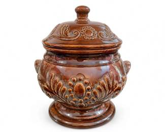 Brown Glazed Ceramic Lidded Canister with Floral Relief
Condition: Good
Decorative brown glazed ceramic canister or sugar jar with matching lid, raised floral/scroll relief, small side handles, and pedestal foot. Condition appears generally good from the front view, though underside, interior, and rim/lid fit are not shown.