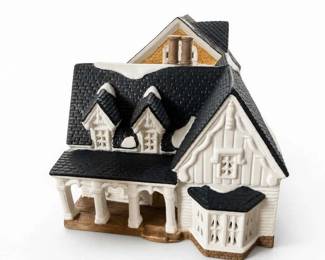 Victorian-style porcelain miniature house collectible display piece
Condition: Good
Decorative porcelain-style miniature house with multiple rooflines, black textured shingles, white molded walls, porch columns, and a bay/windowed front section. Likely intended for seasonal village or display use. No visible lighting or music-box hardware can be confirmed from the image.