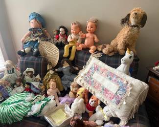 Assorted vintage cloth dolls and plush toy lot
Condition: Fair
Primary salable object is a mixed lot of vintage dolls and stuffed animals, including cloth dolls, baby dolls, and plush toys. Visible items include several seated dolls across the sofa, a stuffed dog, a white unicorn plush, and multiple smaller dolls/toys piled in front. Secondary furniture and textiles are background only and not included as separate items.