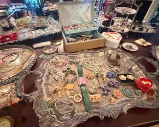 Mixed Vintage Costume Jewelry Tray Lot
Condition: Good
Assorted costume jewelry spread across trays and boxes, including brooches/pins, bead and chain necklaces, clip earrings, rings, bracelets, and small presentation/storage items. Visible pieces include a central green watch/strap item, pearl-like bead strands, turquoise-toned and floral pieces, and multiple mixed-metal fashion items. Secondary trays and boxes are part of the same lot and are not treated as separate salable objects.