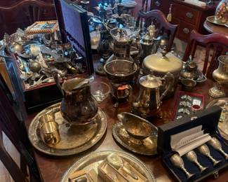 Assorted silverplate tea and serving pieces lot
Condition: Good
Large mixed lot of silverplate table/tea-service and serving items shown grouped on a dining table. Visible are at least several trays or platters, multiple pitchers/creamer-style vessels, lidded bowls, candlesticks, and boxed silver-tone flatware or serving implements. Mixed assortment; not a matching complete service.
