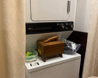 Stacked apartment-size washer and dryer laundry center
Condition: Good
White stacked laundry appliance with a front-hinged upper dryer door, black mid-panel with knobs, and a washer base below. Visible used condition with light surface wear; no obvious major damage is visible from the photo. Curtains partially obscure the sides, and exact brand/model should be confirmed from the data plate or rear/inside door label.