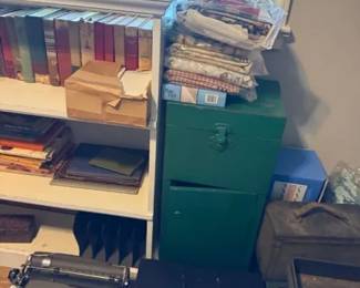 Vintage manual portable typewriter
Condition: Fair
Black vintage portable manual typewriter visible at the lower left of the image, partially obscured by framing and nearby items. Other visible objects include books, a green metal cabinet, and stacked fabric/items, but they are secondary and not treated as separate salable items here.
