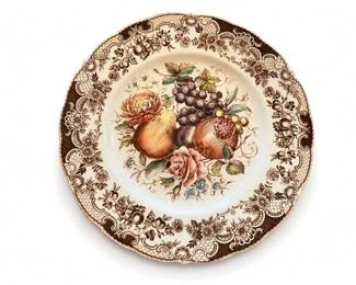 Scalloped ceramic dinner plate with fruit centerpiece and brown floral border
Condition: Good
Round ceramic plate with a scalloped edge, cream ground, brown ornate floral border, and central fruit still-life motif in warm pinks, purples, yellows, and greens. Decorative rather than plain utility ware; likely a dinner or cabinet plate.