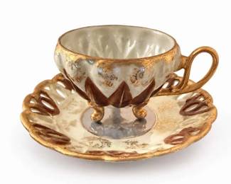 Footed lusterware demitasse cup and saucer set
Condition: Good
Single footed demitasse/tea cup with matching saucer, white-to-cream luster glaze, brown and gold accents, scalloped rims, and decorative openwork handle. Secondary object is only the matching saucer beneath the cup.