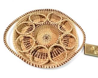 Handwoven round basket tray with six looped compartments
Condition: Good
Round woven basket tray in tan and brown fibers with a central woven well, six attached circular loops around the interior, and a brass-toned rectangular hardware piece on one side. Likely decorative or serving-related; exact intended use is unverified from the image alone.
