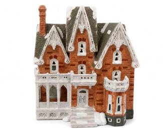 Ceramic Victorian-style miniature house village decoration
Condition: Good
Decorative ceramic miniature house with steep gables, snowy roof treatment, tall chimney, brick-textured walls, bay window sections, and white porch trim. Likely part of a Halloween or Christmas village display. Visible condition appears good from the front, with no obvious major chips seen in the image, though underside and back are not shown.