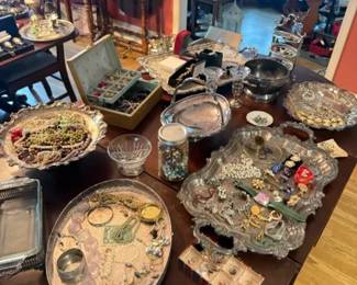 Mixed Estate Costume Jewelry Lot with Ornate Silver-Plated Display Trays
Condition: Good
Assorted estate/costume jewelry including brooches, rings, earrings, necklaces, and small boxed/grouped pieces, plus several ornate silver-plated serving or trinket trays used for display. Condition appears mixed with typical estate wear, and no single maker is identifiable from the photo.