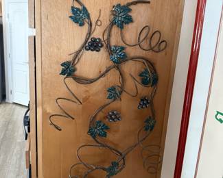 Wine holder decorative wrought iron and metal vine design mounted on a wooden door, featuring clusters of grapes and stylized leaves. The intricate metalwork adds a rustic, vineyard-inspired accent to the interior space.