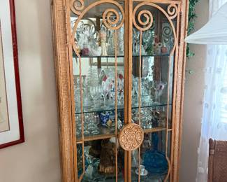 tall wooden china cabinet with glass doors, featuring intricate carved scrollwork and decorative floral accents, displayed in a warmly lit dining room setting.
