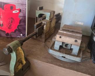 Vintage heavy-duty cast iron mill/drill press swivel vise (right), a long-screw guide clamp/fixture assembly (left/center), and an auxiliary shop heater in box (far left).