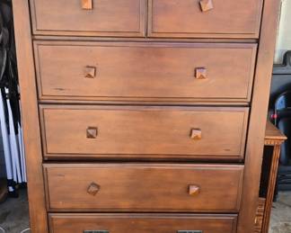 Tall 7-drawer wood chest / highboy dresser with warm brown finish, distinctive geometric wood knobs and metal drop pulls. Generous storage with a relatively compact footprint. Shows surface wear and character from use — great as-is or an excellent refinishing/upcycling piece.