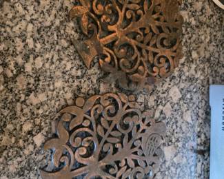 Cast-Iron Tree Trivets — Matching rustic metal trivets featuring an ornate openwork tree design with scrolling branches, leaves and small bird details. Distressed aged-bronze/rust finish gives them a vintage farmhouse or garden-inspired look. Suitable for protecting surfaces from hot cookware or for use as decorative kitchen accents.