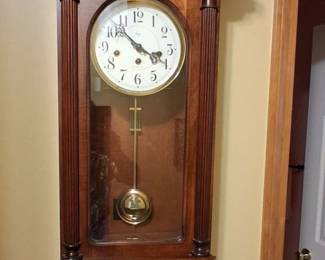 analog chiming clock with a glass door and a visible brass pendulum, resembling models from traditional makers like Howard Miller