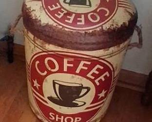 Cylindrical barrel shape featuring a cream and red distressed "Coffee Shop" graphic. Features: Equipped with a padded, removable top lid and side rope handles. Function: Doubles as a small seat/stool and an interior storage compartment.