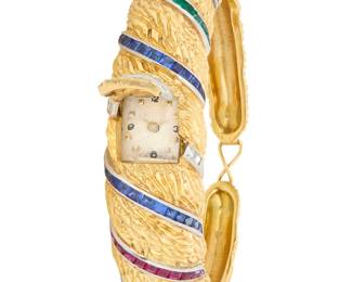 302 A Bi-Color Gold, Ruby, Sapphire, and Diamond Surprise Watch Of a textured domed design featuring alternating bands of channel set rubies, emeralds and sapphires and finished with channel-set French-cut diamonds, dial featuring gold hour markers Inner Circumference: 6 1/2 in. 102.9 grams gross Estimate: $12,000 - $15,000