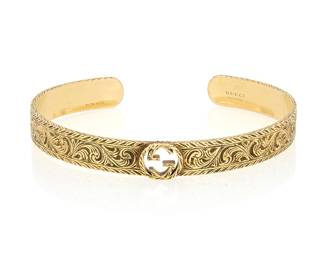 16 Gucci: An 18K Gold Bangle Featuring a scrolling engraved design centering an interlocking 'G', signed Gucci, with Italian workshop marks Inner Circumference: 5 3/4 in., Gap: 7/8 in. 20.4 grams gross Estimate: $3,000 - $5,000