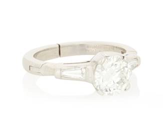 50 A Platinum and Diamond Ring Centering a round brilliant-cut diamond weighing 1.11 carats, flanked by two tapered baguette diamonds Size: 4 with a hinged shank 4.9 grams gross Accompanied by a GIA Report numbered #2231994777, dated July 06, 2026, stating the diamond as Natural with a color grade of G and a clarity grade of SI2, no fluorescence. Estimate: $1,500 - $2,500