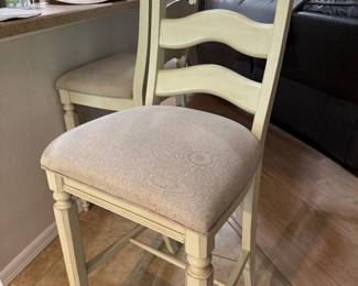 COASTAL UPHOLSTERED BAR-HEIGHT STOOLS — PAIR: Soft Cream Finish • Neutral Upholstered Seats • Sculpted Ladder Backs • Turned-Leg Detailing • Metal Footrest Protectors • Casual Coastal / Transitional Style