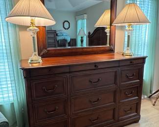 TOMMY BAHAMA–STYLE TROPICAL RESORT KING BEDROOM COLLECTION: Rich Warm-Wood Finish • Dovetail Drawer Construction • Carved Tropical Leaf Accents • Statement Panel Bed • Beveled Mirror • Coordinating Case Pieces: King Panel Bed Arched Headboard • Panel Footboard • Turned Posts & Finials • Wood Side Rails Dresser & Beveled Mirror Dovetail Drawers • Carved Tropical Leaf Accents • 12 Drawers Tall 5-Drawer Chest Dovetail Drawer Construction • Rich Warm-Wood Finish • 6 Drawers Two 2-Drawer Nightstands Dovetail Drawer Construction