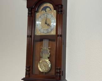 Traditional Mahogany-Finish Pendulum Wall Clock w/ Moon-Phase Dial: Ornate brass-tone dial, decorative columns, glass-front case and pendulum.