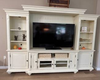 LARGE 3-PIECE LIGHTED ENTERTAINMENT WALL UNIT Coastal Transitional Entertainment Center • Distressed Cream/Ivory Finish • Oversized Center TV Console & Bridge • Two Matching Lighted Display Towers • Adjustable Display Shelving • Paneled Backing • Generous Enclosed Storage • Glass-Front Media Components • Decorative Crown Molding • Coordinating Furniture-Style Feet