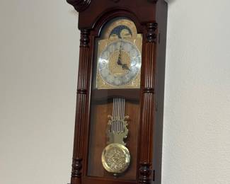 Traditional Mahogany-Finish Pendulum Wall Clock w/ Moon-Phase Dial: Ornate brass-tone dial, decorative columns, glass-front case and pendulum.